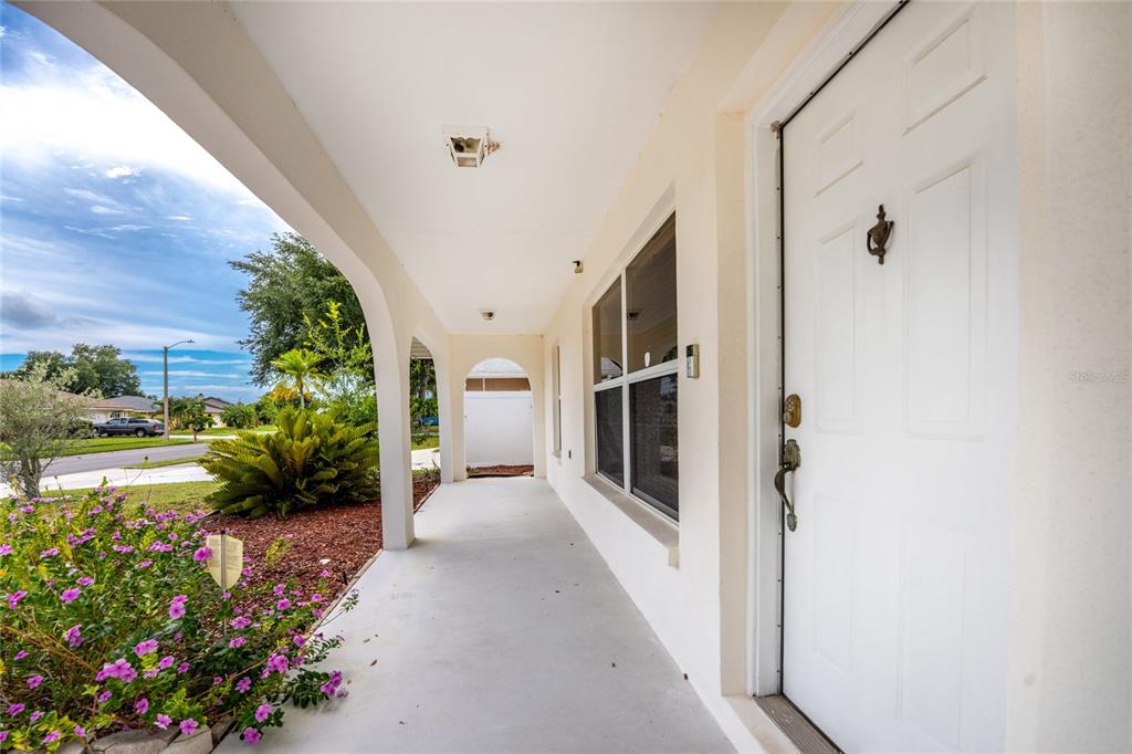 A covered front porch features a white door, a window, and a garden with flowers — 1458 STRADA D ARGENTO, VENICE, FL