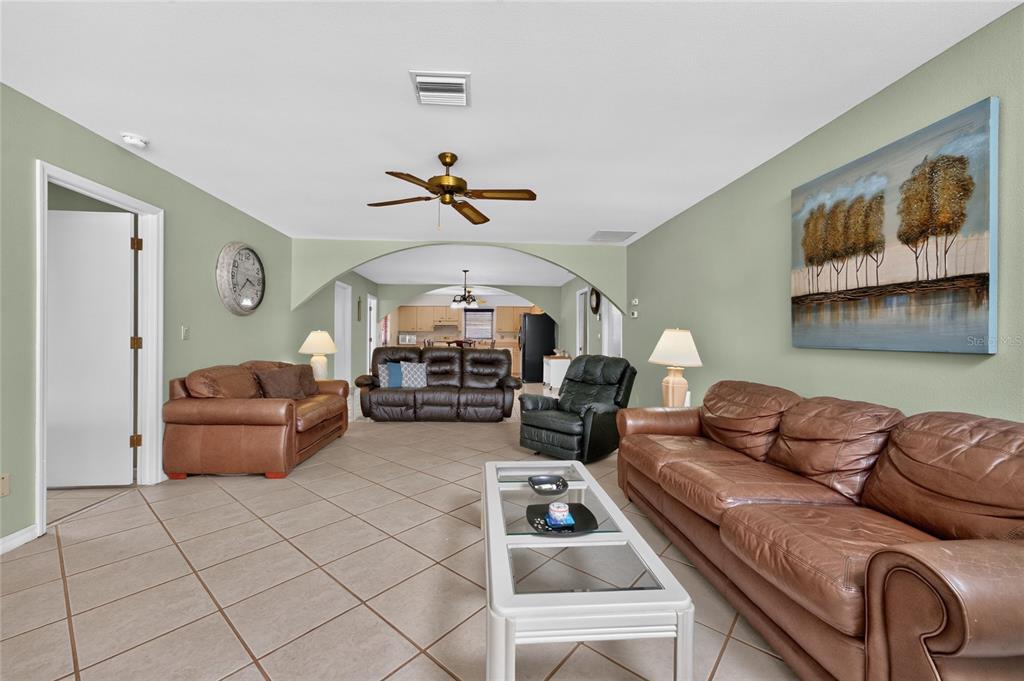 A living room features tile flooring, leather furniture, and an arched opening to the kitchen — 1458 STRADA D ARGENTO, VENICE, FL
