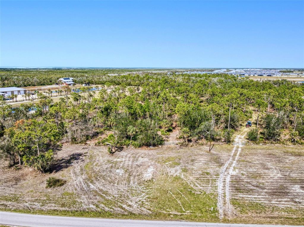 An aerial view shows a cleared lot with a dirt path leading into a wooded area — 24552 YACHT CLUB BOULEVARD, PUNTA GORDA, FL