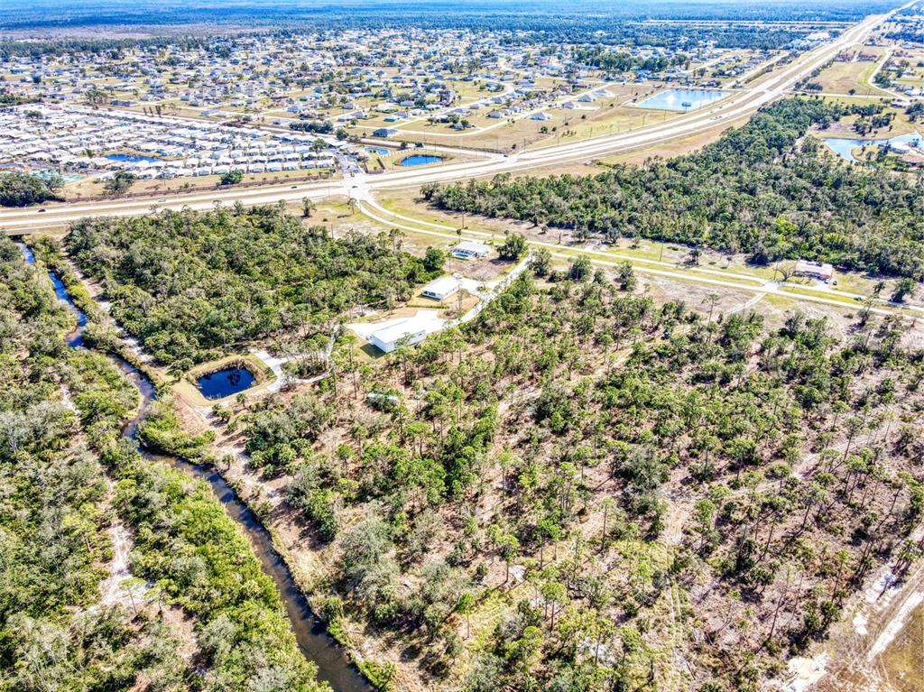 An aerial view shows a rural property with a house, pond, and surrounding wooded land — 24552 YACHT CLUB BOULEVARD, PUNTA GORDA, FL