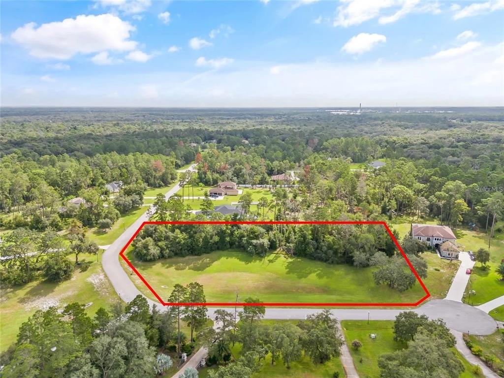 An aerial view shows a vacant, grassy residential lot outlined in red within a wooded neighborhood — 13615 GOPHER POND CT, HUDSON, FL