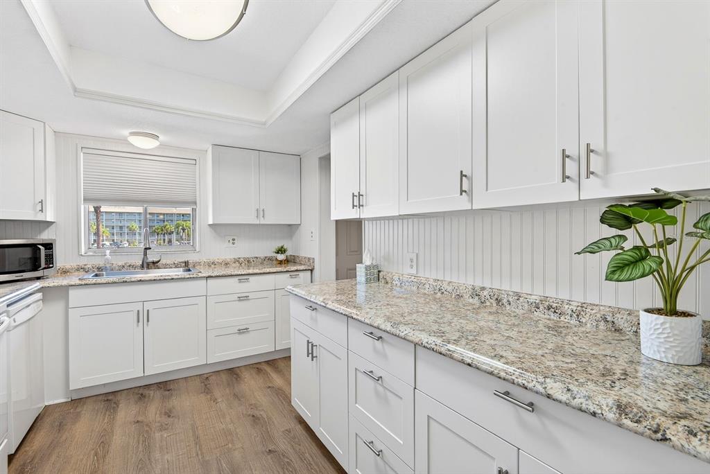 A kitchen features white cabinets, granite countertops, a sink, and wood-look flooring — 3344 LAKE BAYSHORE DRIVE UNIT P205, BRADENTON, FL