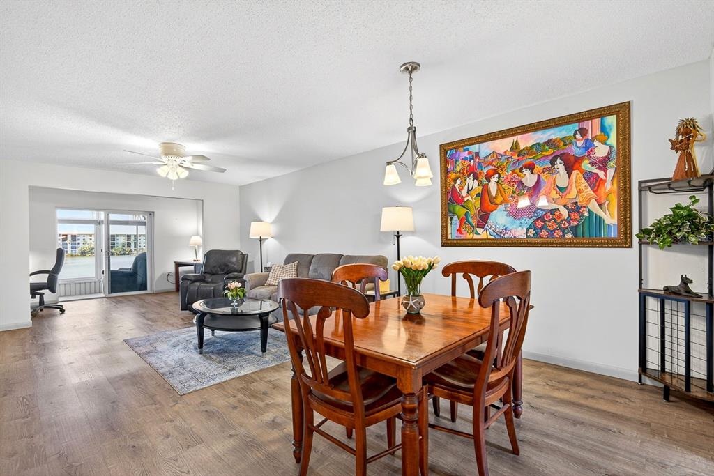 A dining area and living room with wood-look flooring, a large colorful painting, and balcony — 3344 LAKE BAYSHORE DRIVE UNIT P205, BRADENTON, FL