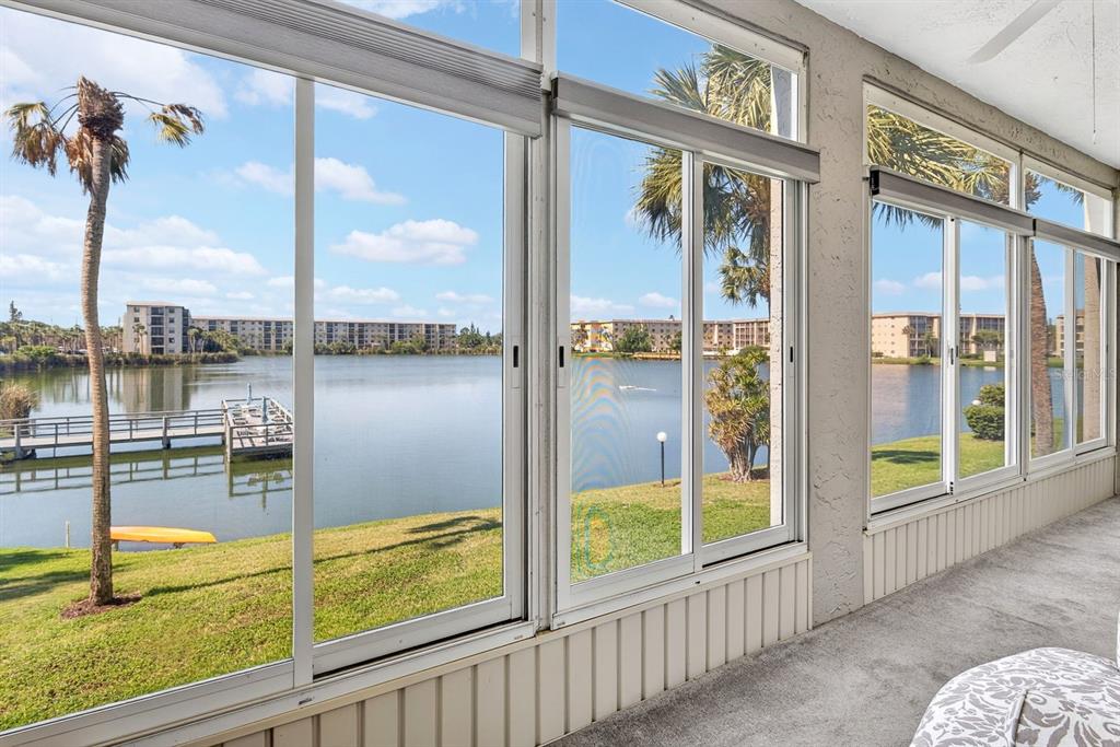 A sunroom with large windows overlooking a lake, a wooden dock, and palm trees — 3344 LAKE BAYSHORE DRIVE UNIT P205, BRADENTON, FL