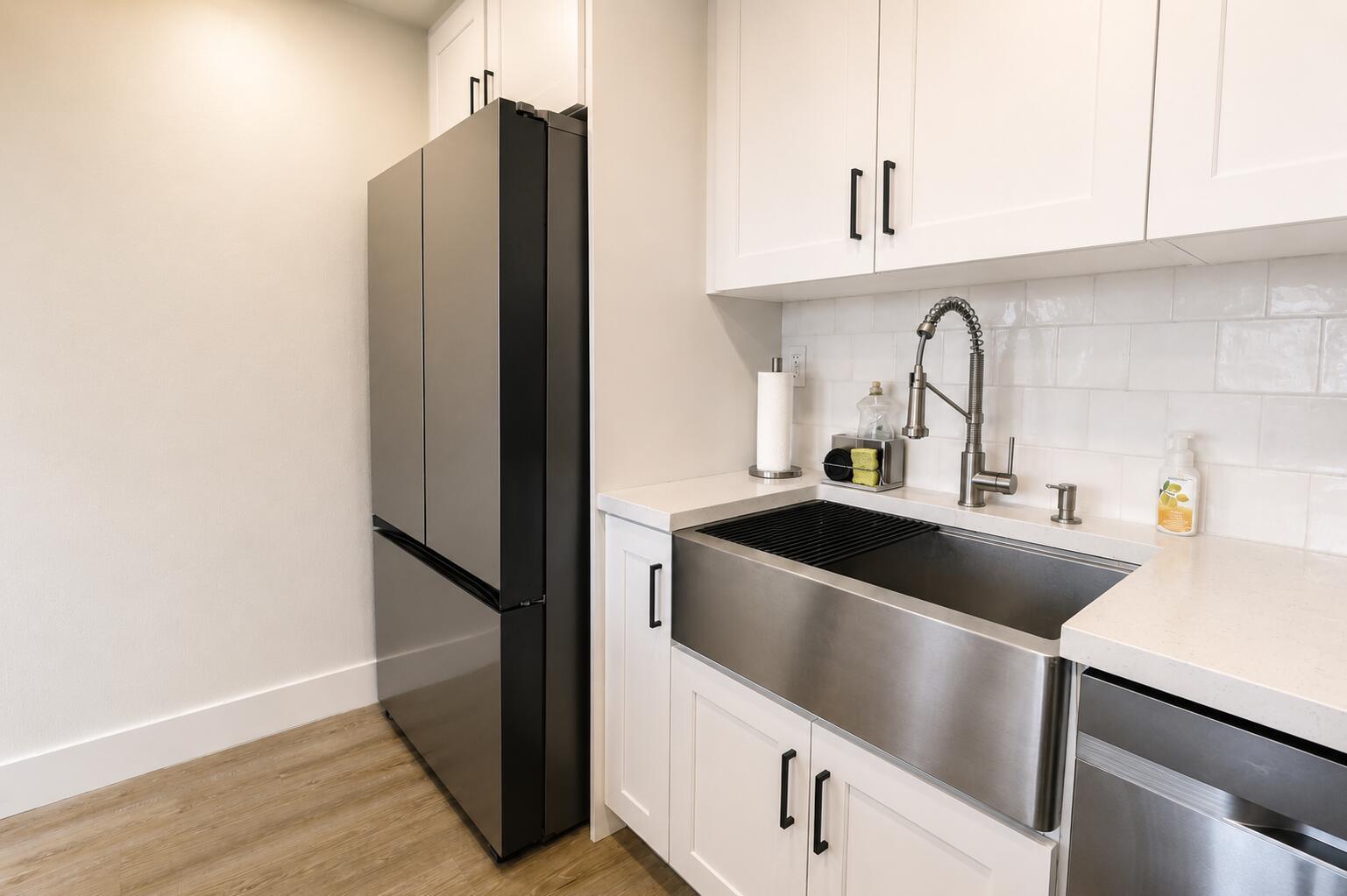 A modern kitchen features a stainless steel farmhouse sink, white cabinets, and a black refrigerator — 9491 Evergreen Place # 307, Davie FL 33324, DAVIE, FL