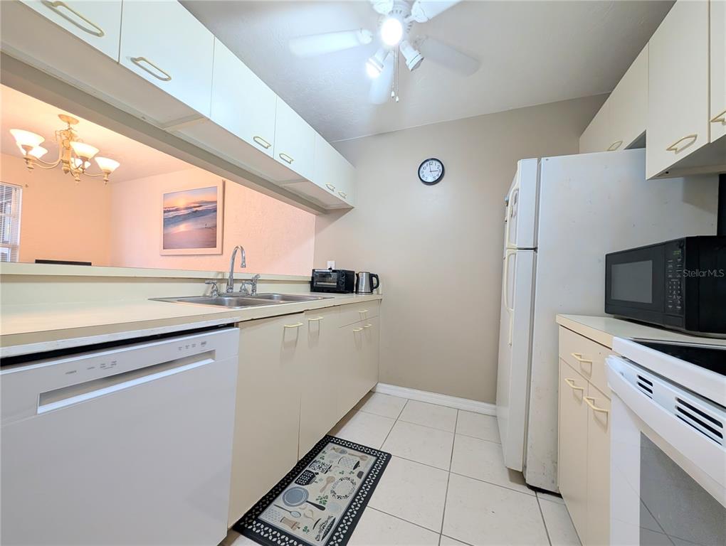 A galley-style kitchen features white cabinets, light-colored tile flooring, and a pass-through window — 3609 59TH AVENUE W UNIT 3609, BRADENTON, FL