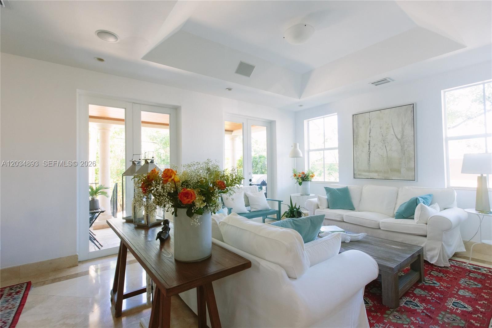 A bright living room features white sofas, a wooden coffee table, and a red rug — 335 W Enid Dr, Key Biscayne FL 33149, KEY BISCAYNE, FL