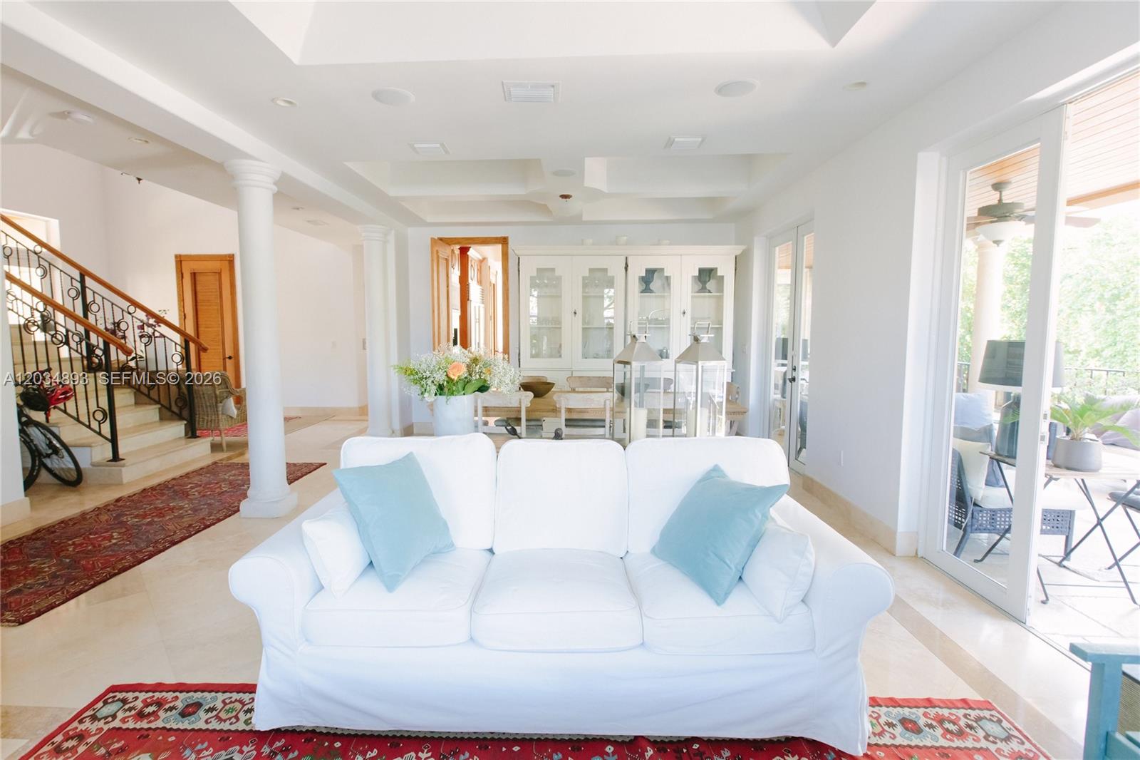 A white sofa sits in a living room featuring a staircase, columns, and dining area — 335 W Enid Dr, Key Biscayne FL 33149, KEY BISCAYNE, FL