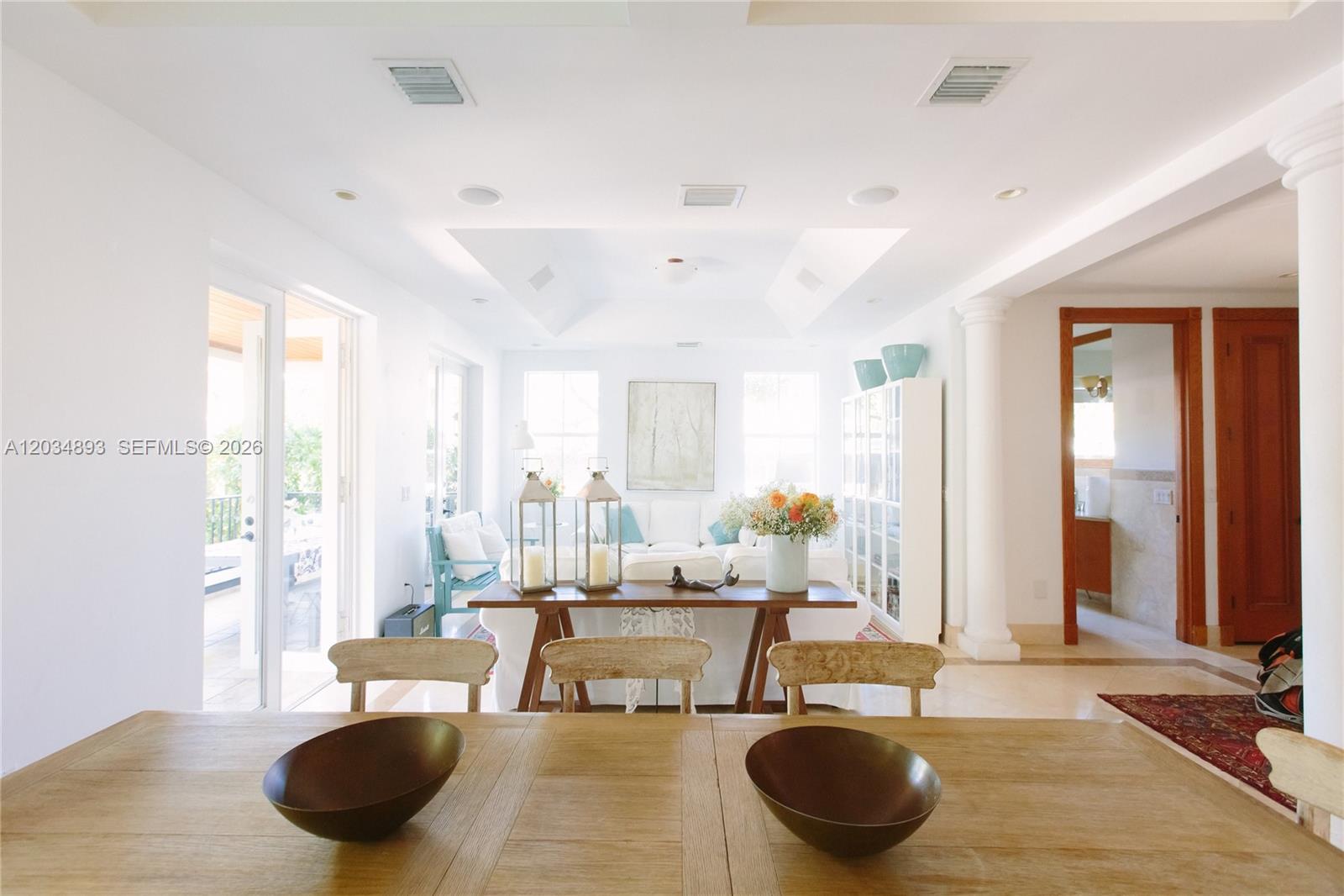 A dining area with wooden bowls in the foreground opens into a bright living room — 335 W Enid Dr, Key Biscayne FL 33149, KEY BISCAYNE, FL
