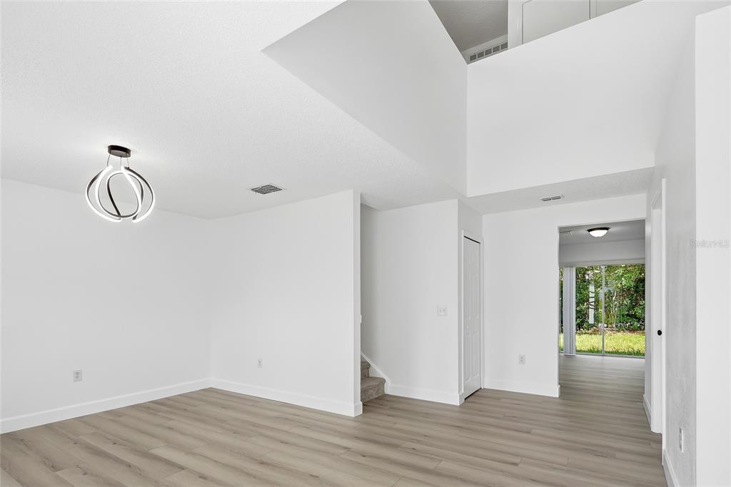 A bright, empty room features light wood-look flooring, a modern pendant light, and high ceilings — 5292 DENVER AVE, SPRING HILL, FL