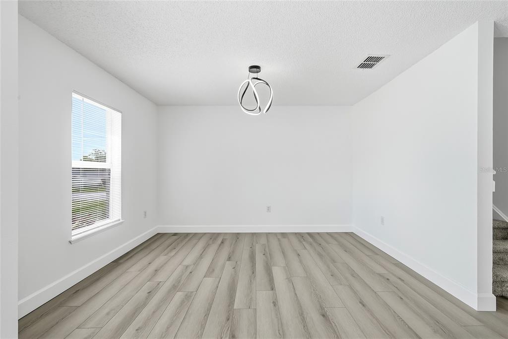 A bright dining room features white walls, light wood-look flooring, and a modern circular light fixture — 5292 DENVER AVE, SPRING HILL, FL