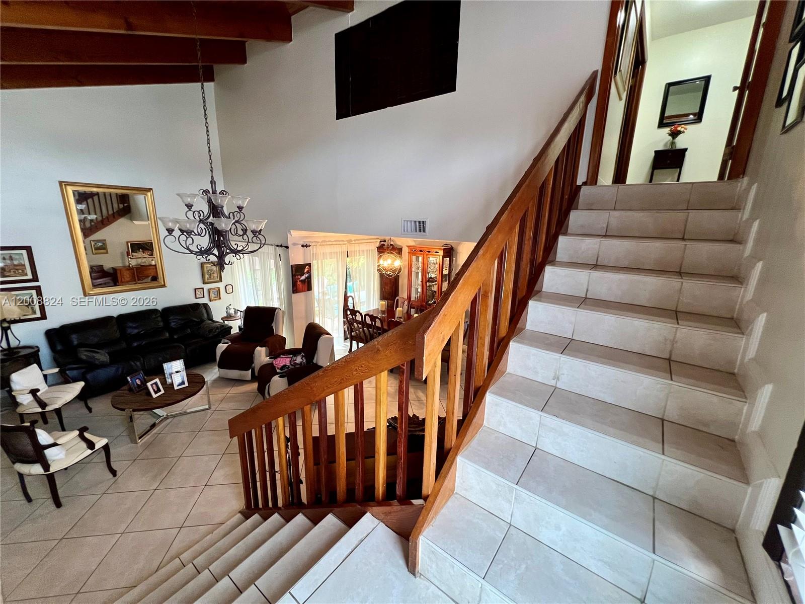 A tiled staircase with a wooden railing overlooks a living room with vaulted ceilings — 3610 SW 113th Pl, Miami FL 33165, MIAMI, FL