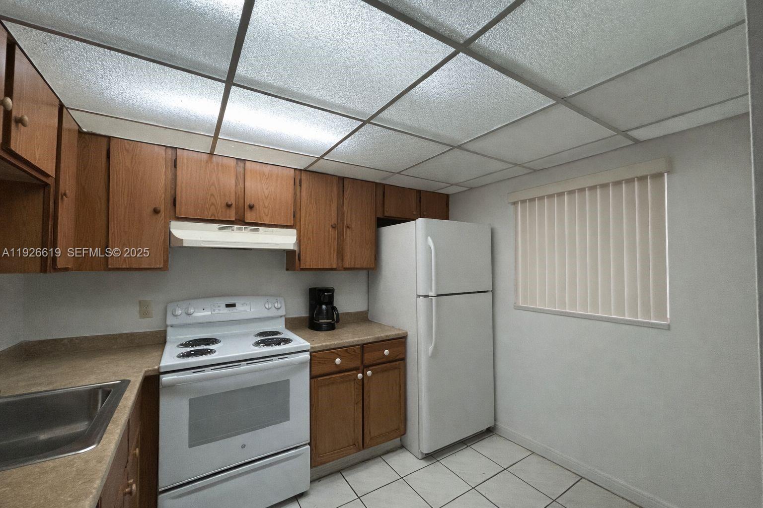 A kitchen features wood cabinets, white appliances, a drop ceiling, and light-colored tile flooring — 19701 SW 114th Ave # 14, Miami FL 33157, MIAMI, FL