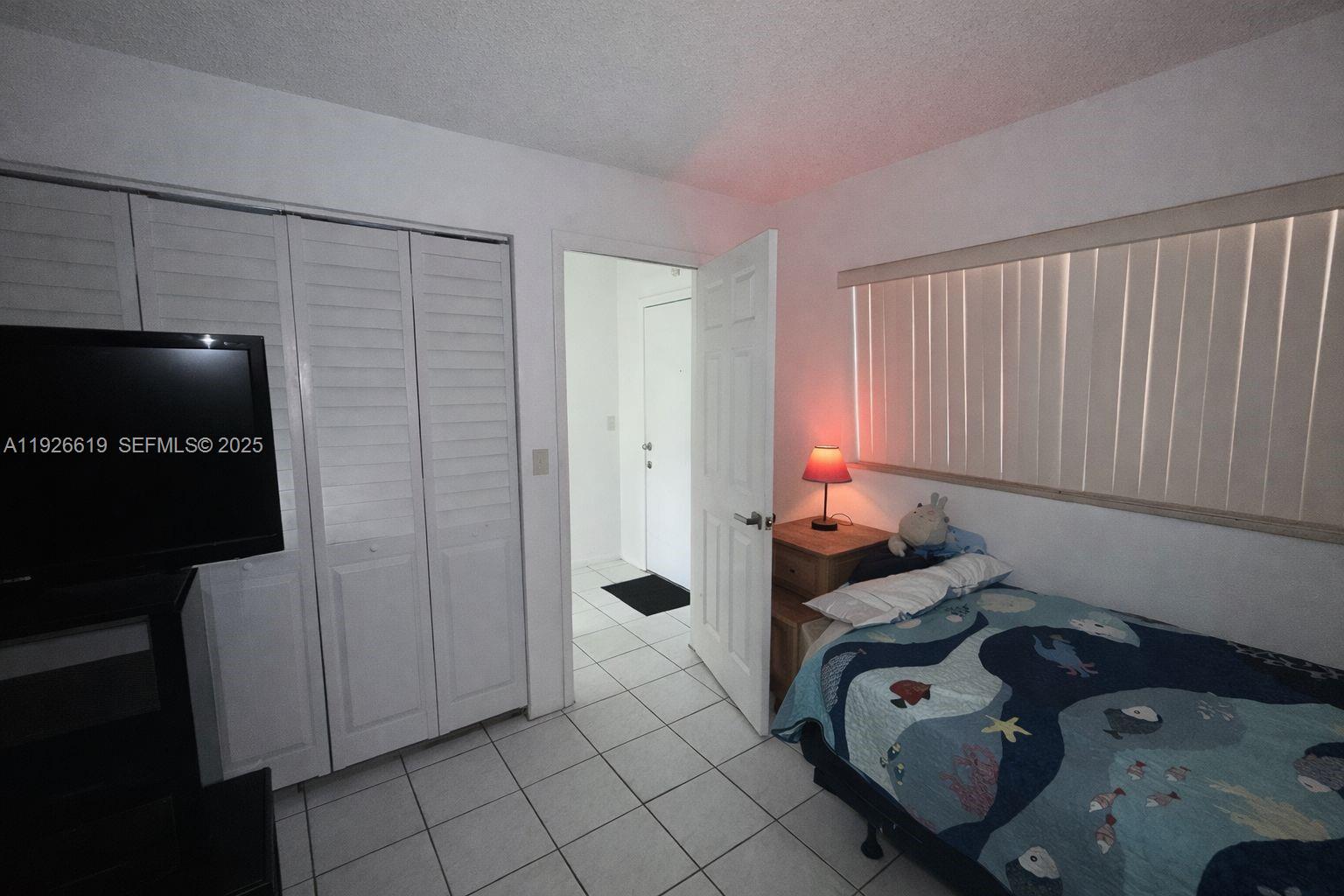 A bedroom features a single bed, a television, a closet, and white tile flooring — 19701 SW 114th Ave # 14, Miami FL 33157, MIAMI, FL