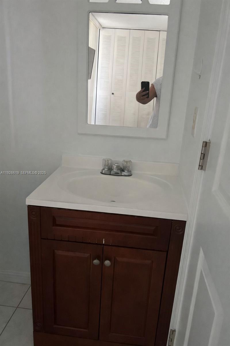 A bathroom features a dark wood vanity with a white sink and a wall mirror — 19701 SW 114th Ave # 14, Miami FL 33157, MIAMI, FL