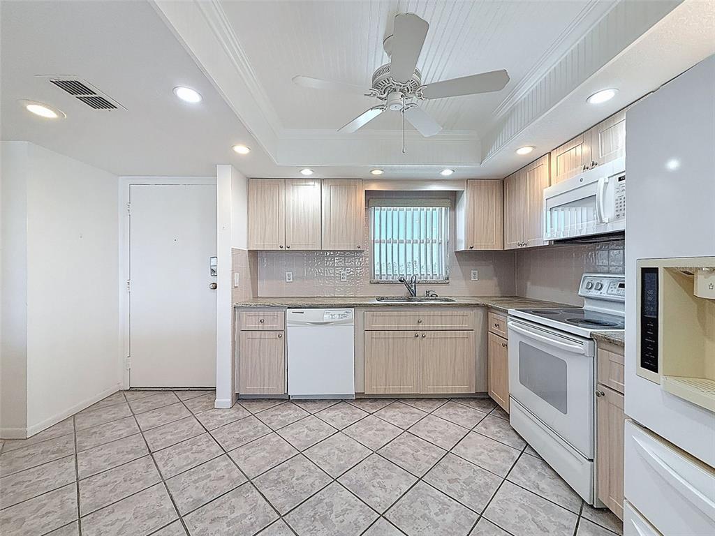 A kitchen features light wood cabinets, white appliances, tile flooring, and a ceiling fan — 4550 COVE CIRCLE UNIT 507, ST PETERSBURG, FL