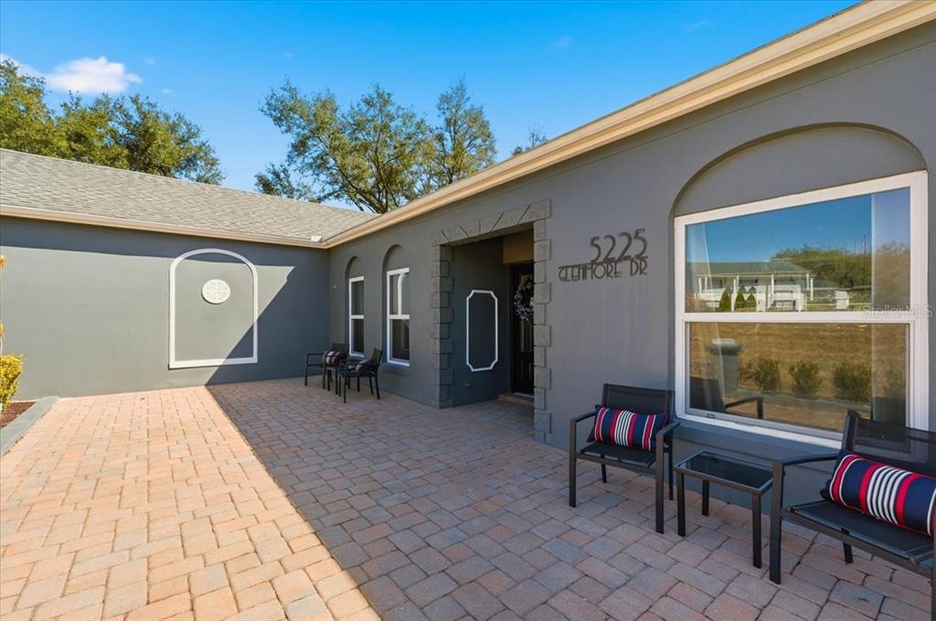 A paved patio sits in front of a gray house with a large window — 5225 GLENMORE DRIVE, LAKELAND, FL