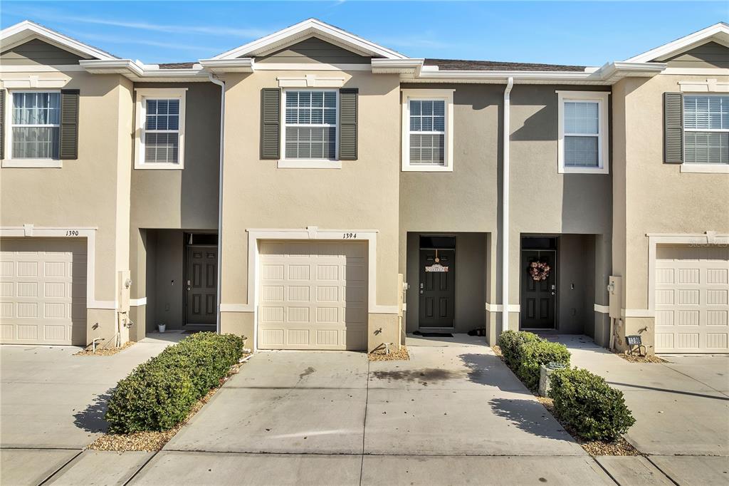 A row of tan townhouses features attached garages, front entry doors, and small landscaped bushes — 1394 YELLOW FINCH DRIVE, DAVENPORT, FL