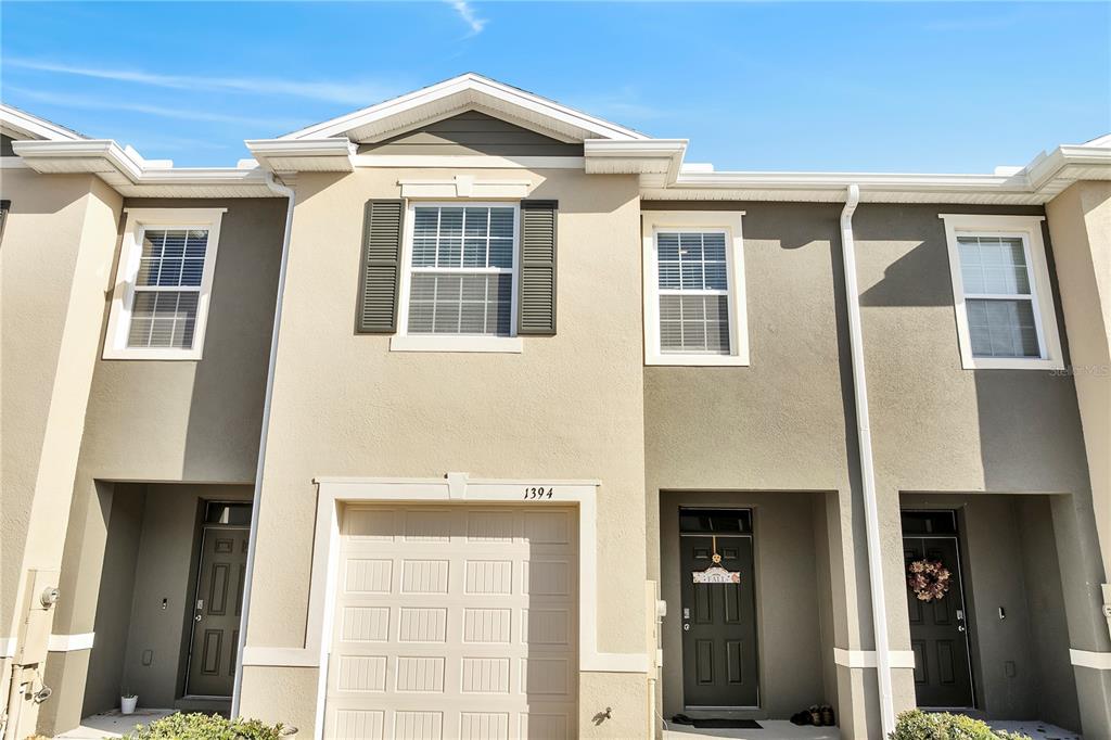 A two-story townhouse exterior features a single-car garage, tan stucco walls, and dark shutters — 1394 YELLOW FINCH DRIVE, DAVENPORT, FL