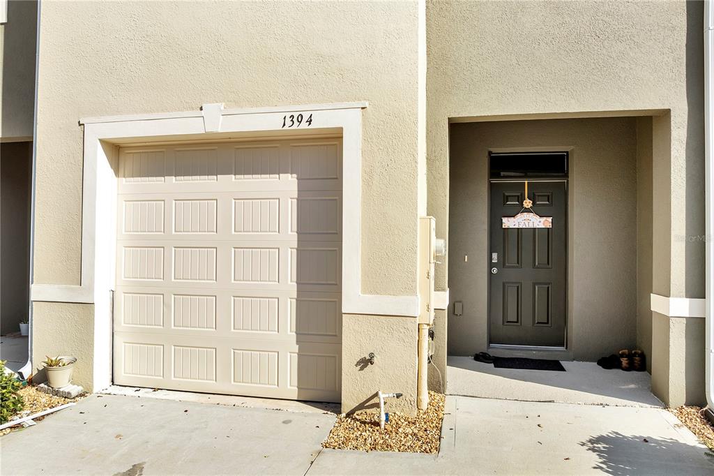 A beige townhouse exterior features a single-car garage and a dark front door — 1394 YELLOW FINCH DRIVE, DAVENPORT, FL