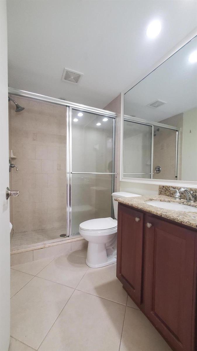A bathroom features a glass-enclosed shower, a white toilet, and a vanity with granite countertops — 1727 HIGHWAY A1A Highway # 106, Vero Beach FL 32963, VERO BEACH, FL