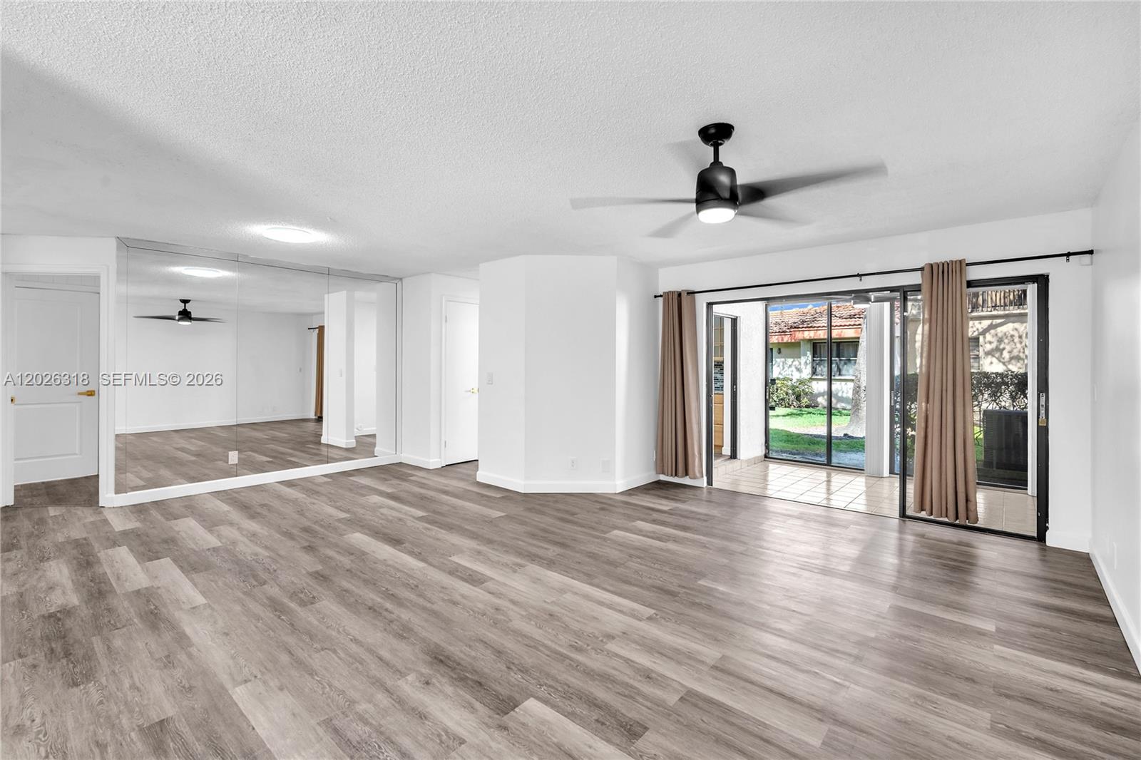 A living room features wood-look flooring, a mirrored wall, a ceiling fan, and sliding glass doors — 3405 Emerald Oaks Dr # 00, Hollywood FL 33021, HOLLYWOOD, FL