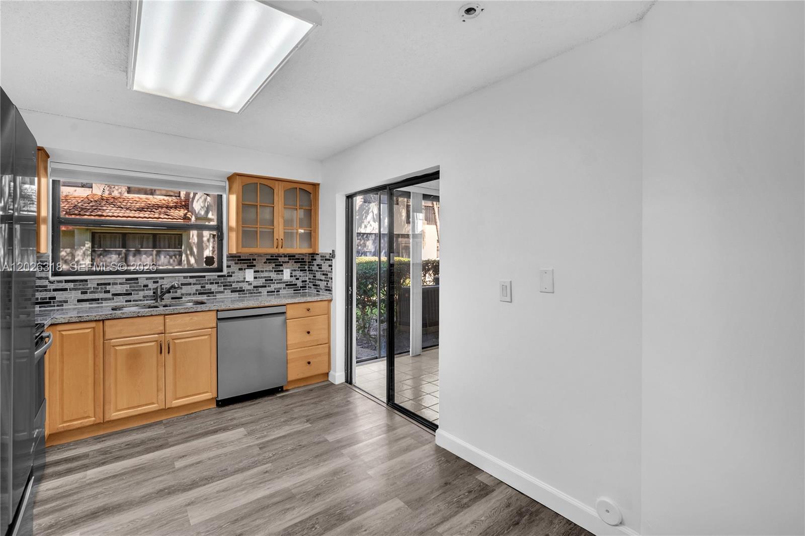 A kitchen features light wood cabinets, gray laminate flooring, a tile backsplash, and sliding glass doors — 3405 Emerald Oaks Dr # 00, Hollywood FL 33021, HOLLYWOOD, FL