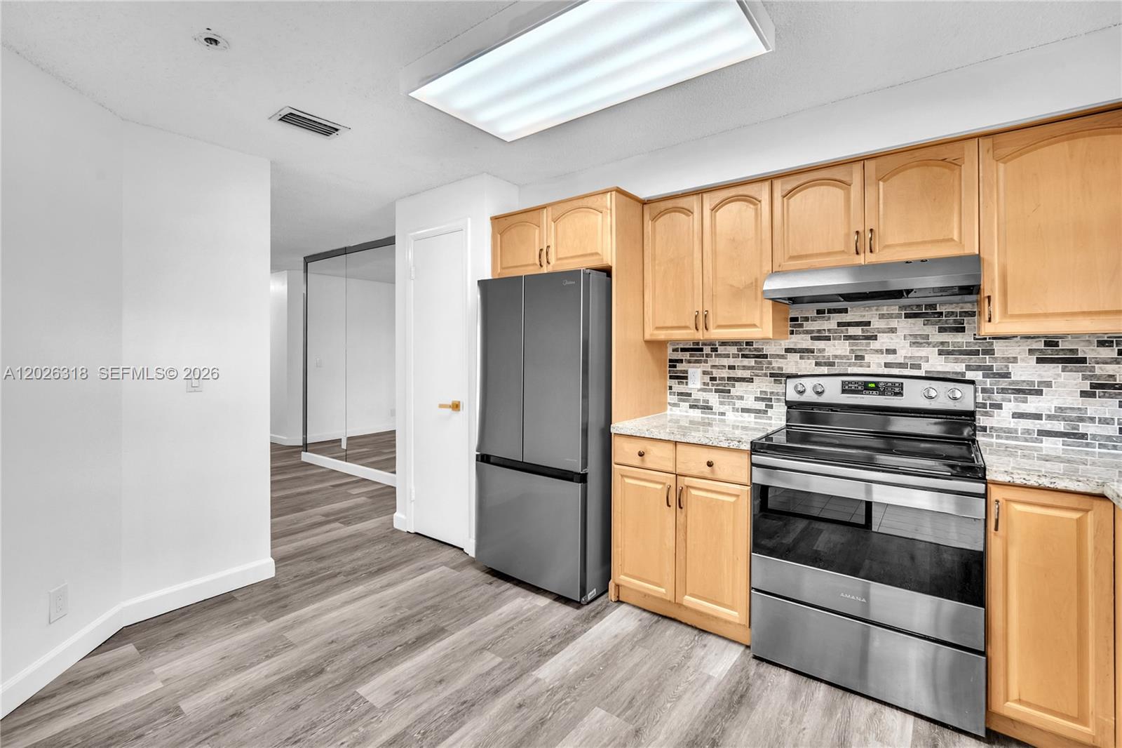 A kitchen features light wood cabinets, stainless steel appliances, and a gray tiled backsplash — 3405 Emerald Oaks Dr # 00, Hollywood FL 33021, HOLLYWOOD, FL