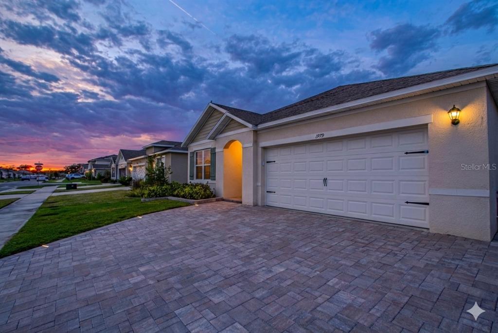 A single-story suburban house with a paved driveway and a two-car garage at sunset — 1979 CACUTTA WAY, KISSIMMEE, FL