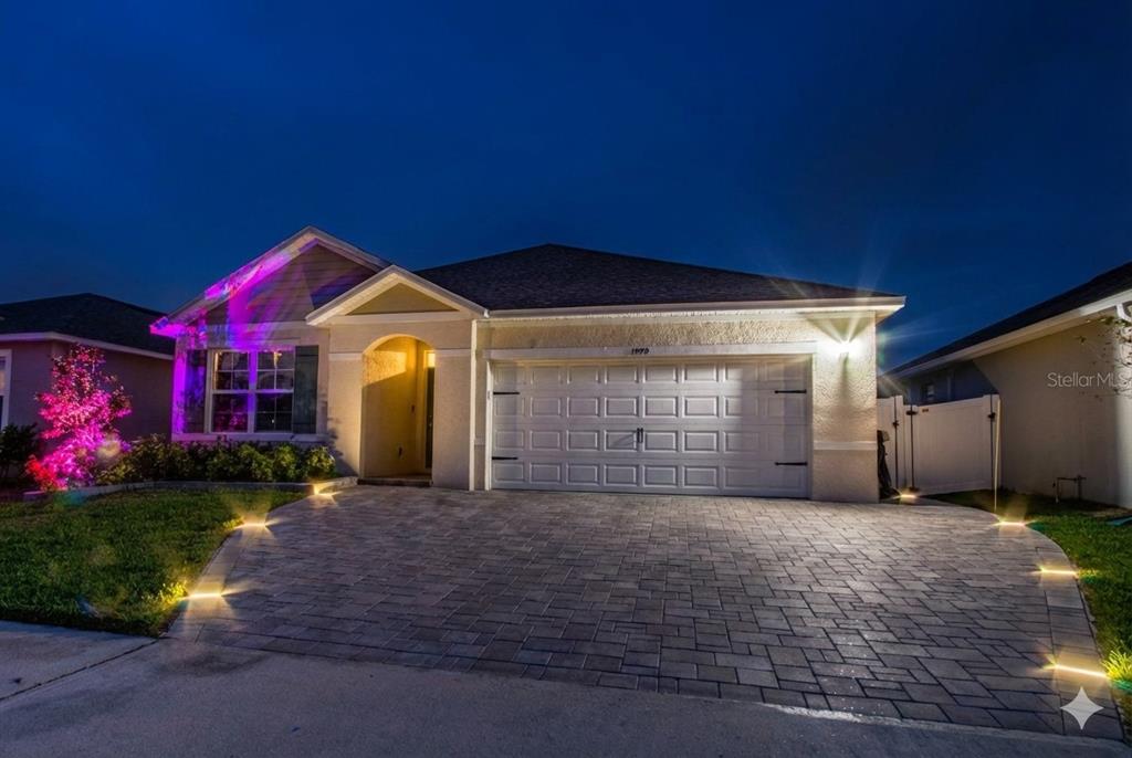 A single-story house with a paved driveway, exterior lighting, and a two-car garage at night — 1979 CACUTTA WAY, KISSIMMEE, FL