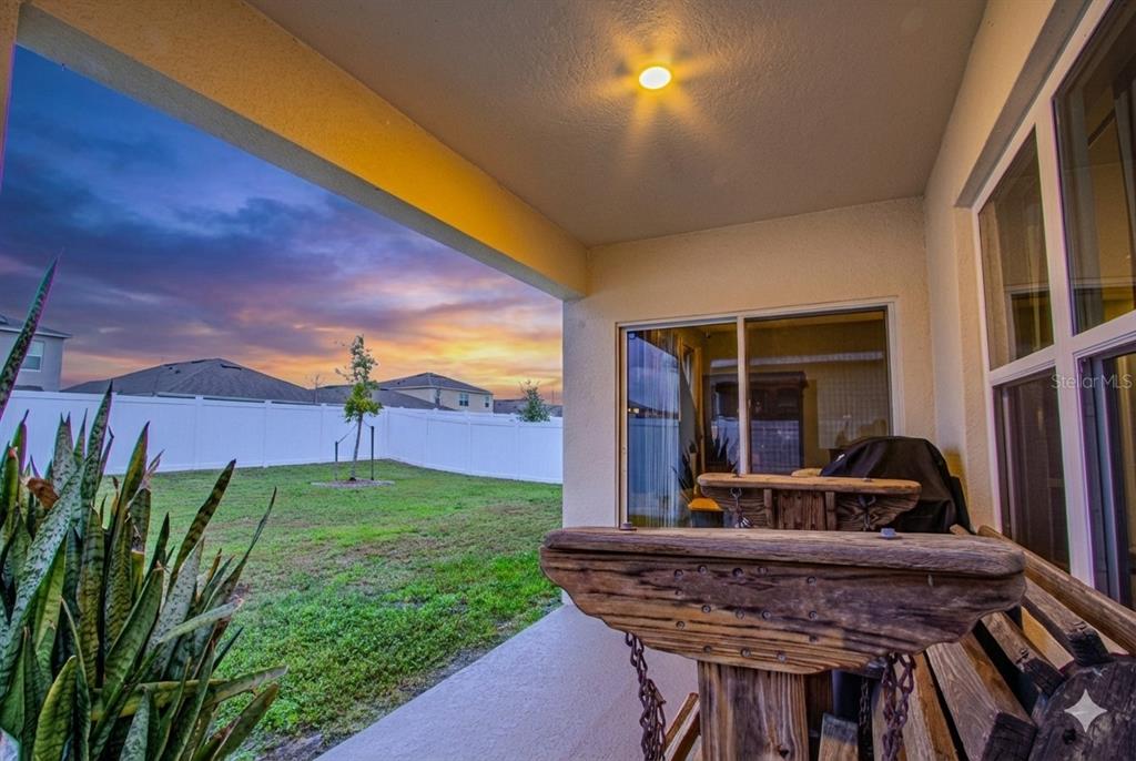 A covered patio overlooks a grassy backyard with a white fence at sunset — 1979 CACUTTA WAY, KISSIMMEE, FL