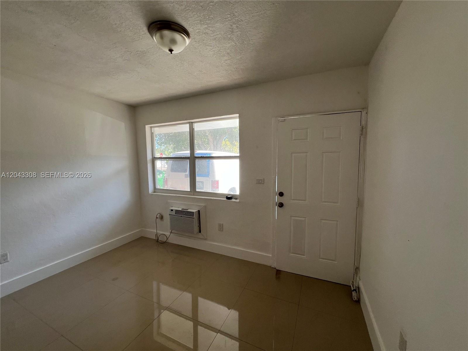 A room with white walls, tile flooring, a window air conditioner, and a white door — MIAMI, FL