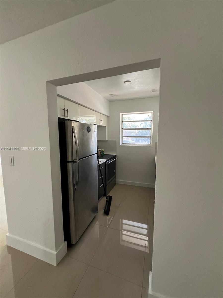 A galley-style kitchen features stainless steel appliances, white upper cabinets, and light-colored tile flooring — MIAMI, FL