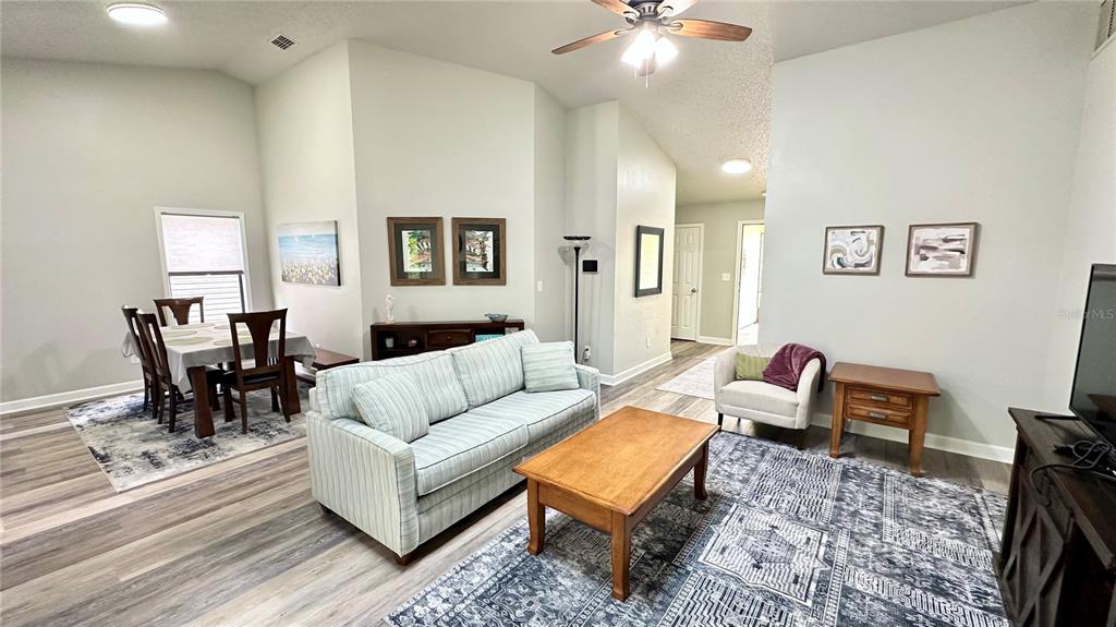This living and dining area features vaulted ceilings, light-colored walls, and wood-look flooring — 782 PINE SHORES CIRCLE, NEW SMYRNA BEACH, FL