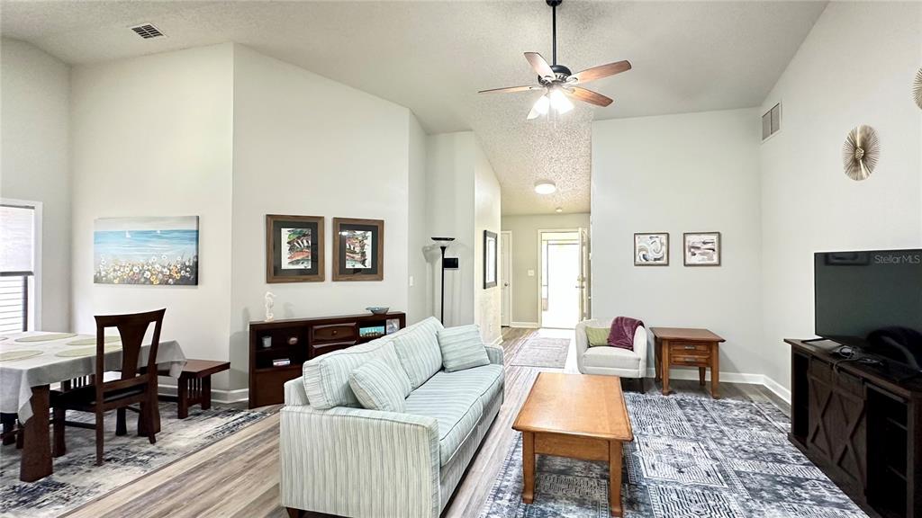A living room with a sofa, coffee table, television, and dining area on wood-look flooring — 782 PINE SHORES CIRCLE, NEW SMYRNA BEACH, FL