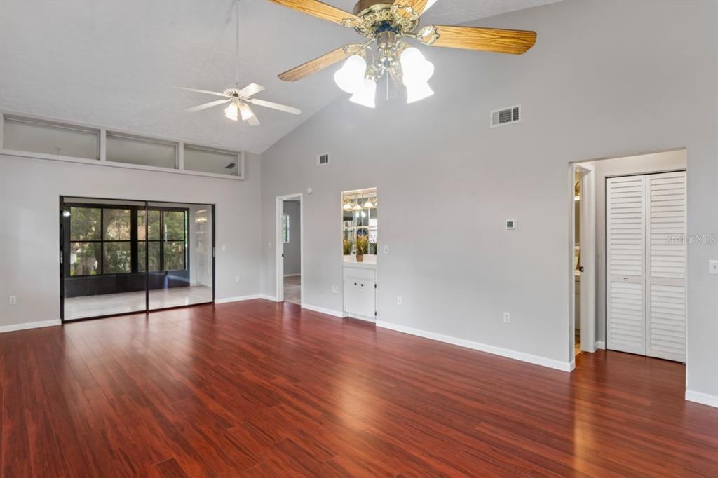A spacious living room features vaulted ceilings, wood-look flooring, two ceiling fans, and sliding doors — 8550 SHADBLOW CT UNIT #6, PORT RICHEY, FL