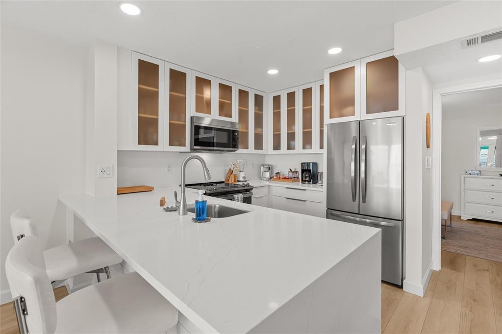 A modern kitchen features white cabinets, stainless steel appliances, and a white quartz breakfast bar — 711 BEACH ROAD UNIT 408, SARASOTA, FL