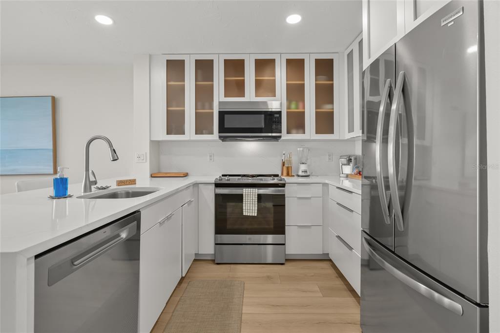 A modern kitchen features white cabinets, stainless steel appliances, and a white quartz countertop — 711 BEACH ROAD UNIT 408, SARASOTA, FL