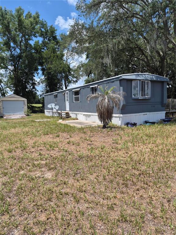 A gray mobile home features a wooden deck and a bay window under oak trees — 9285 SE 140TH PLACE, SUMMERFIELD, FL