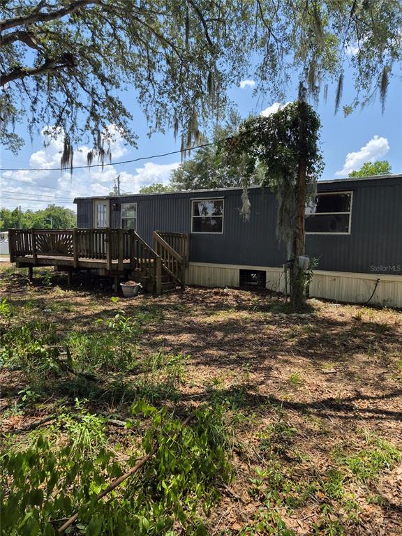 A dark-sided mobile home sits on a dirt lot with a wooden deck attached — 9285 SE 140TH PLACE, SUMMERFIELD, FL
