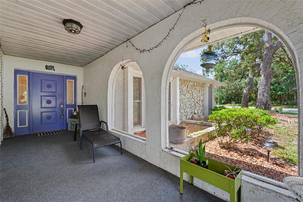 A covered porch features a purple front door, arched openings, and a lounge chair — 8251 EARLSHIRE LANE, SPRING HILL, FL