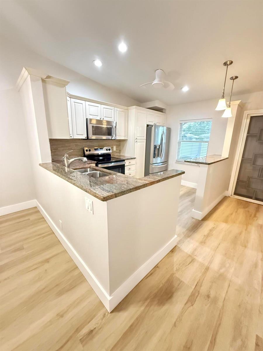 A kitchen features white cabinets, granite countertops, stainless steel appliances, and light wood flooring — 18765 Candlewick Drive, Boca Raton FL 33496, BOCA RATON, FL
