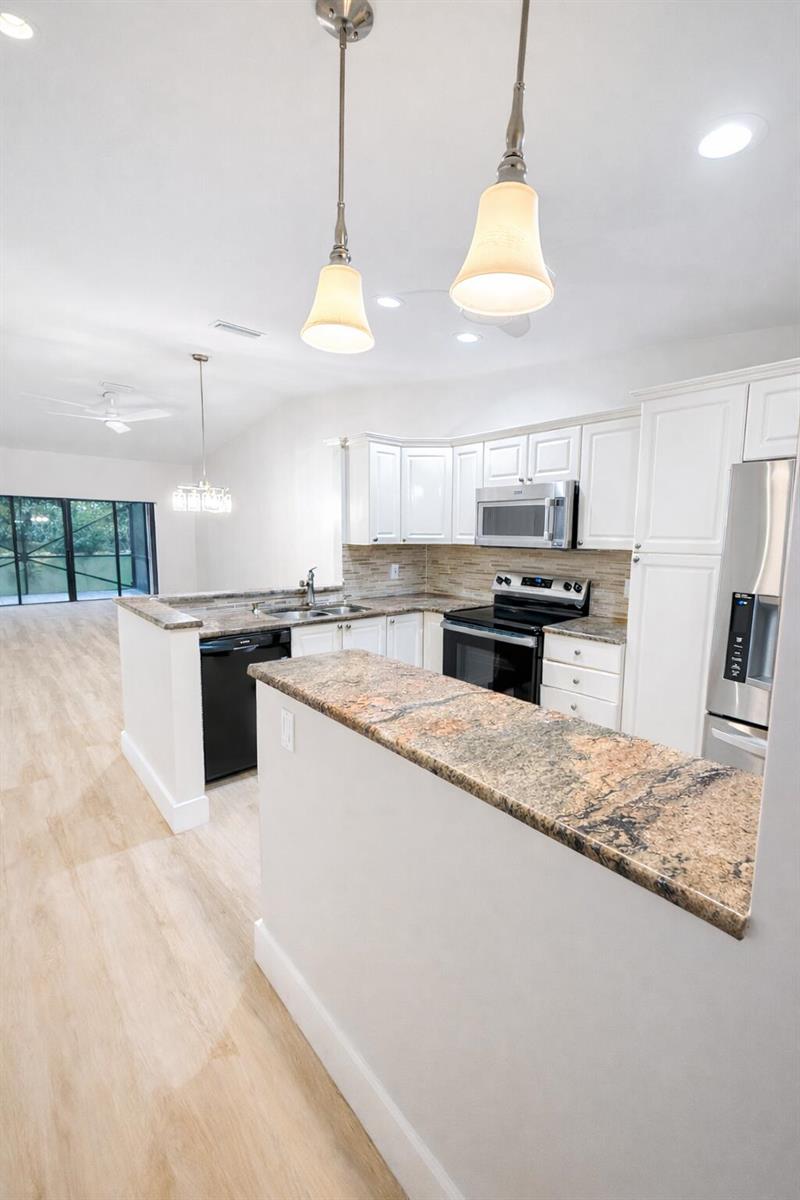 A kitchen features white cabinets, granite countertops, stainless steel appliances, and light wood-look flooring — 18765 Candlewick Drive, Boca Raton FL 33496, BOCA RATON, FL