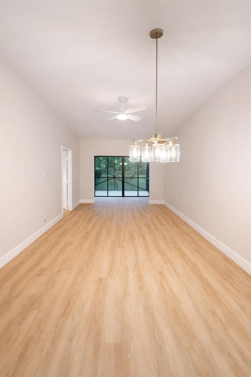 An empty room features light wood-look flooring, a modern chandelier, and a ceiling fan — 18765 Candlewick Drive, Boca Raton FL 33496, BOCA RATON, FL