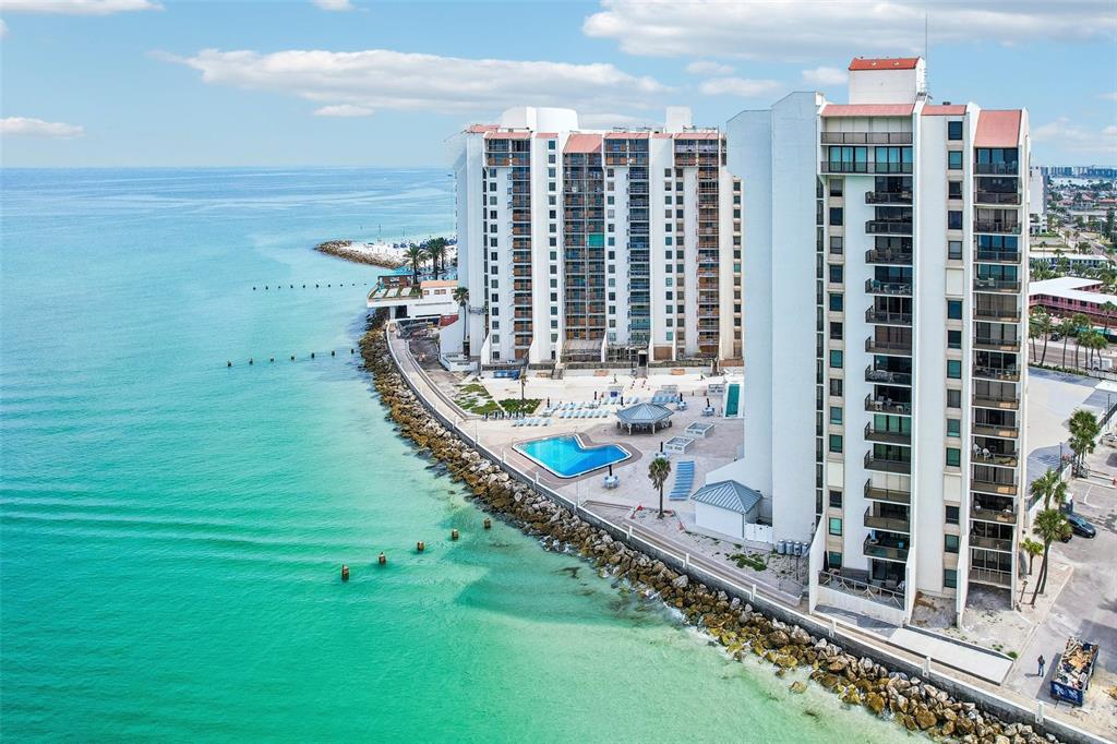 An aerial view of a beachfront high-rise condominium complex with a pool and rocky shoreline — 450 S GULFVIEW BOULEVARD UNIT 605, CLEARWATER BEACH, FL