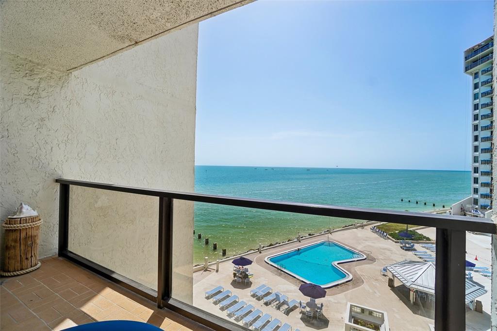 A balcony view overlooking a swimming pool, a sandy beach, and the ocean — 450 S GULFVIEW BOULEVARD UNIT 605, CLEARWATER BEACH, FL