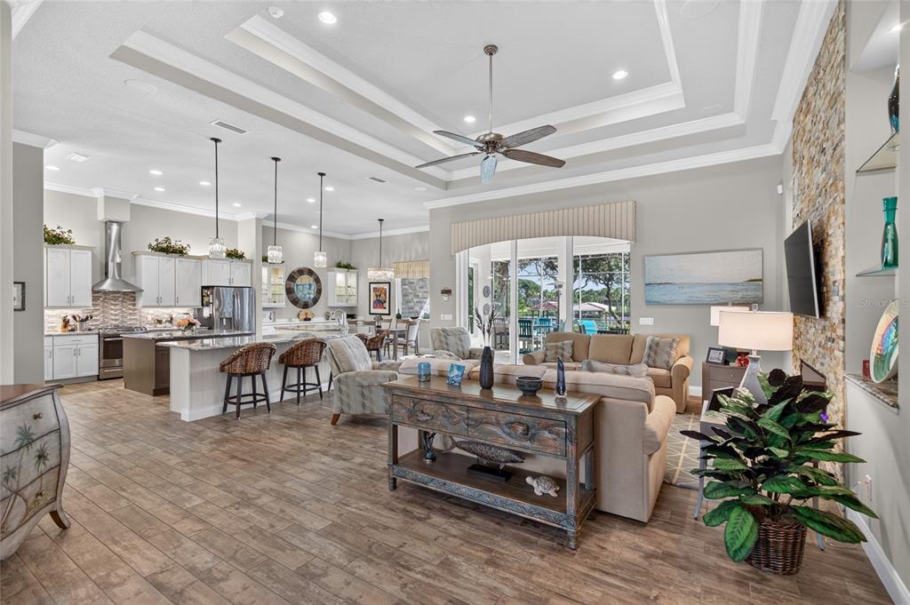 An open-concept living room and kitchen featuring a tray ceiling, stone fireplace, and tile flooring — 28 N WATERVIEW DRIVE, PALM COAST, FL