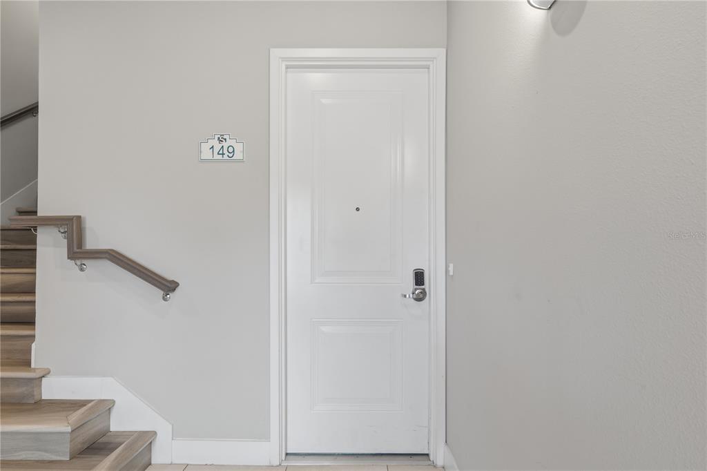 A white door with a digital lock and unit number 149 sits beside a staircase — 7740 SANDY RIDGE DRIVE UNIT 149, REUNION, FL
