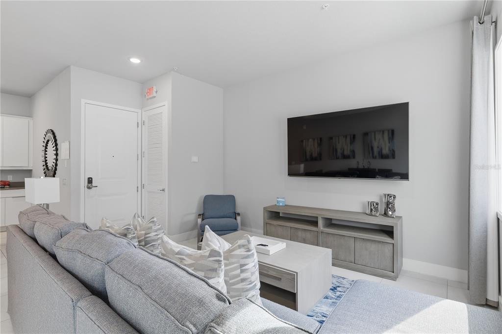 A living room features a gray sectional sofa, a wall-mounted television, and a media console — 7740 SANDY RIDGE DRIVE UNIT 149, REUNION, FL