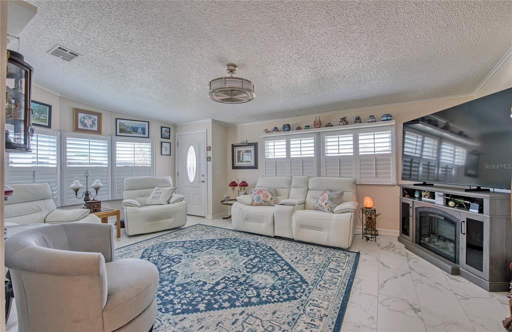A living room features white leather furniture, a blue patterned rug, and a large television — 214 DOLPHIN DRIVE N, OLDSMAR, FL